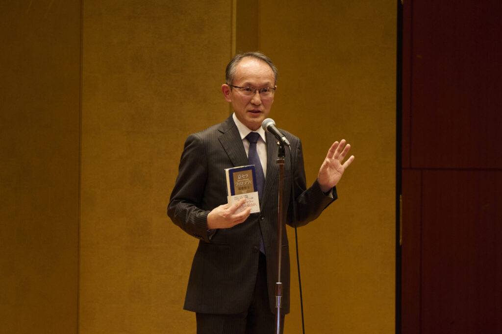 壇上で「京セラフィロソフィ」の書籍を手に、社員たちへスピーチをする西脇社長