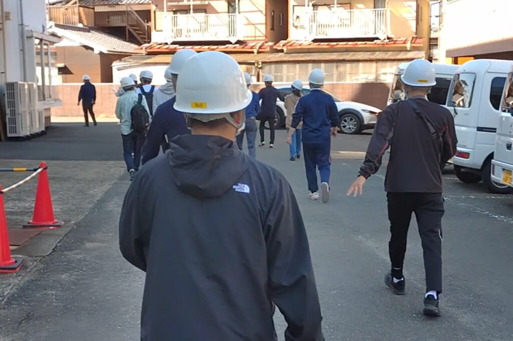 建物の裏口から駐車場を通り集合場所へ向かう避難訓練中の社員たち